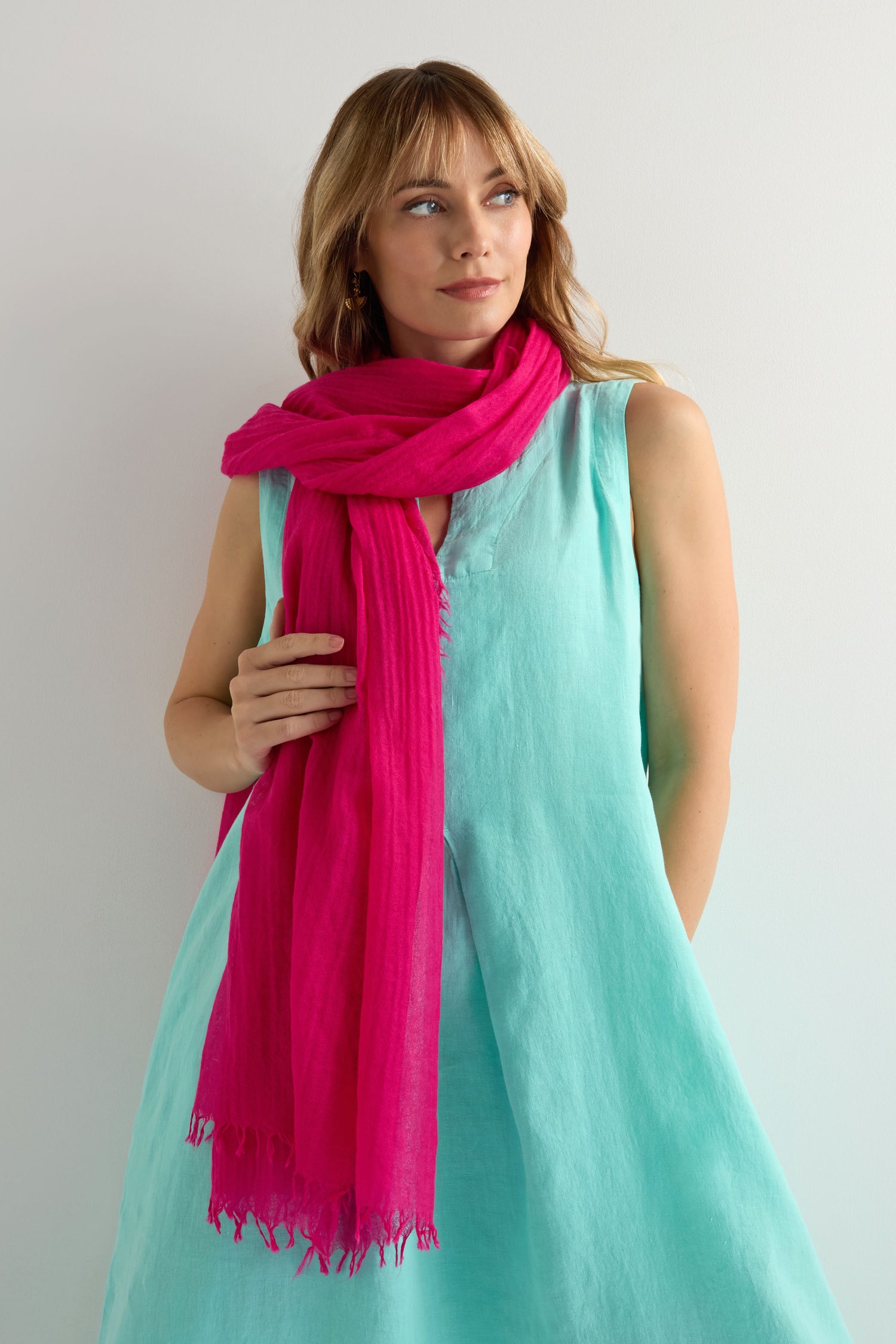 Woman in a sleeveless light blue dress styles the Hibiscus Fine Wool Fringe Scarf, standing against a plain light-colored background.