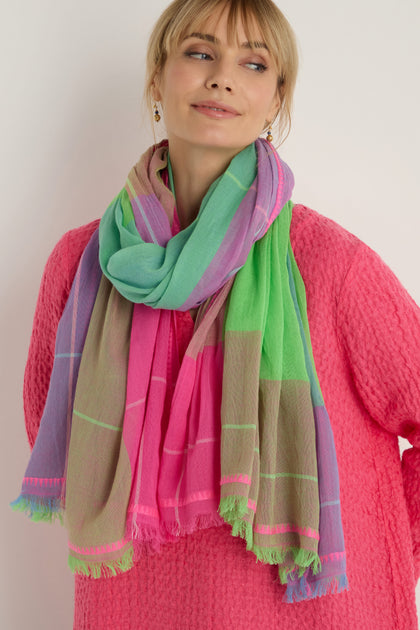 A woman stands against a plain background wearing a textured pink top and the Embroidered Colour Pop Check Cotton Scarf, featuring bold green, pink, beige, and purple sections.