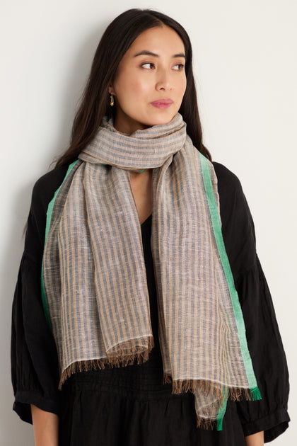 A woman in a black dress and the Spearmint Trim Soft Stripe Scarf stands against a plain light wall, looking slightly to the side.