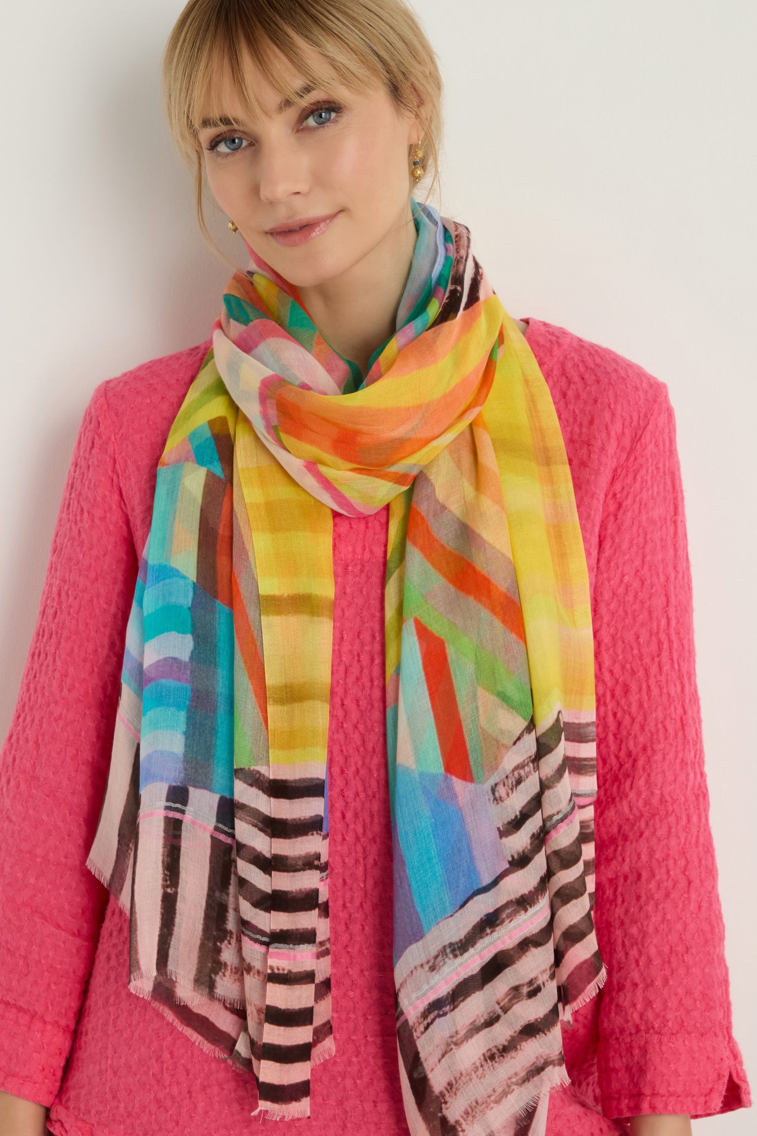 A woman stands against a white background wearing a textured pink top and the Directional Stripe Modal Blend Scarf.