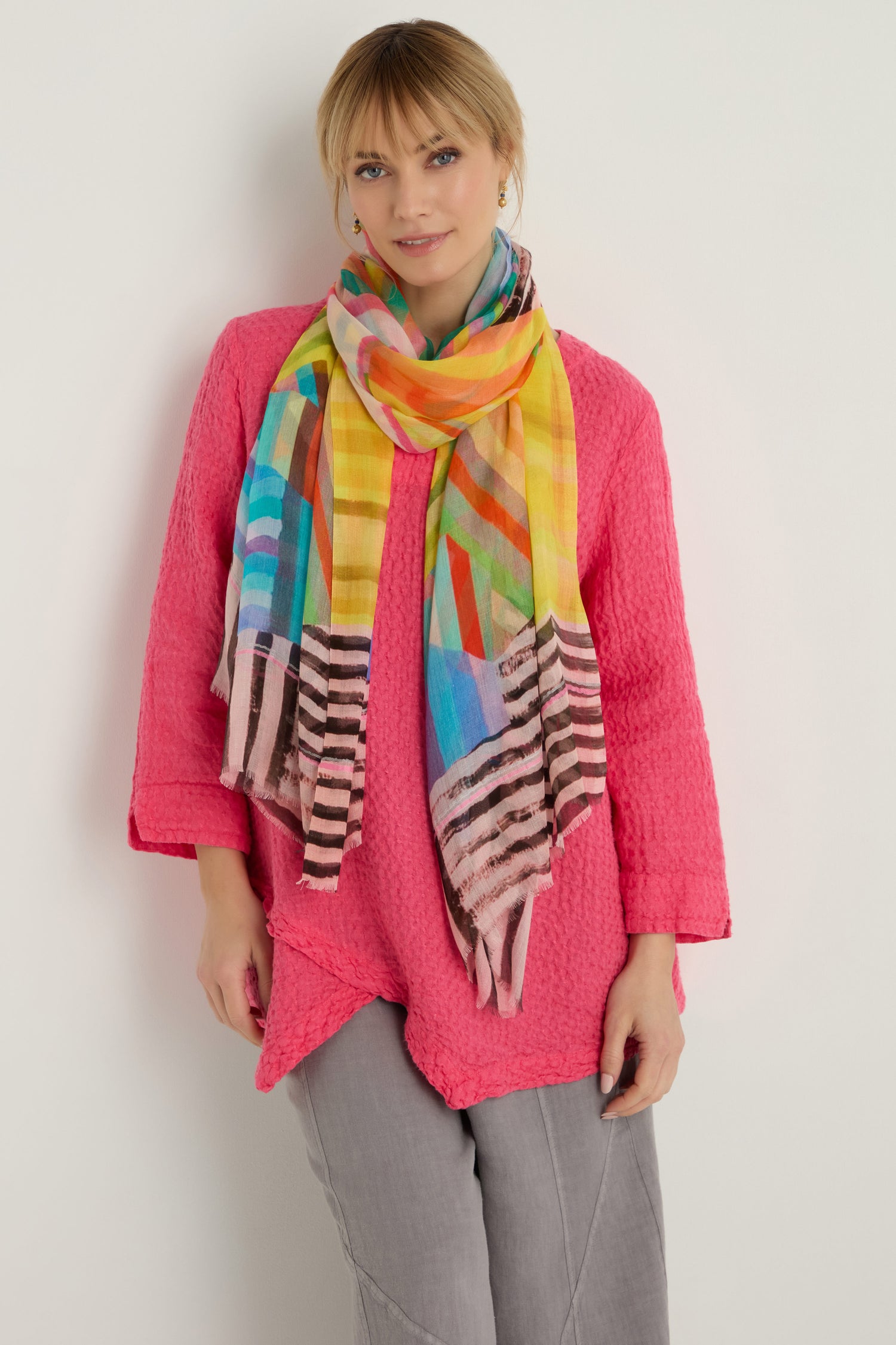 A person stands against a plain light background wearing a textured pink long-sleeve top, light gray pants, and the Directional Stripe Modal Blend Scarf.