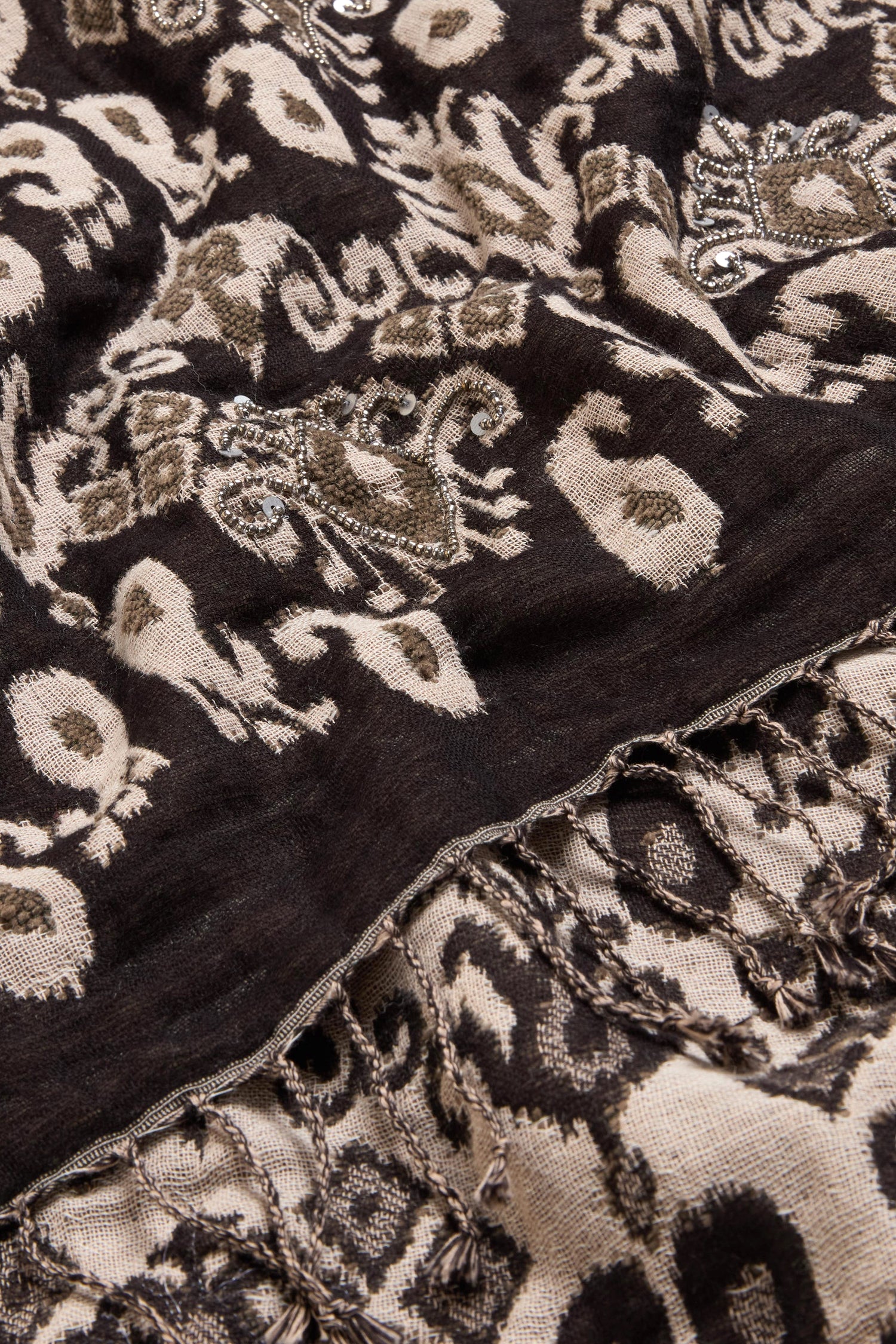 Close-up of the Motif Sequin Scarf, showcasing an abstract black and beige pattern in a neutral palette with decorative embroidery, subtle metallic sequins, and fringed edges. Crafted from a soft cotton-wool blend, this piece exudes effortless sophistication.