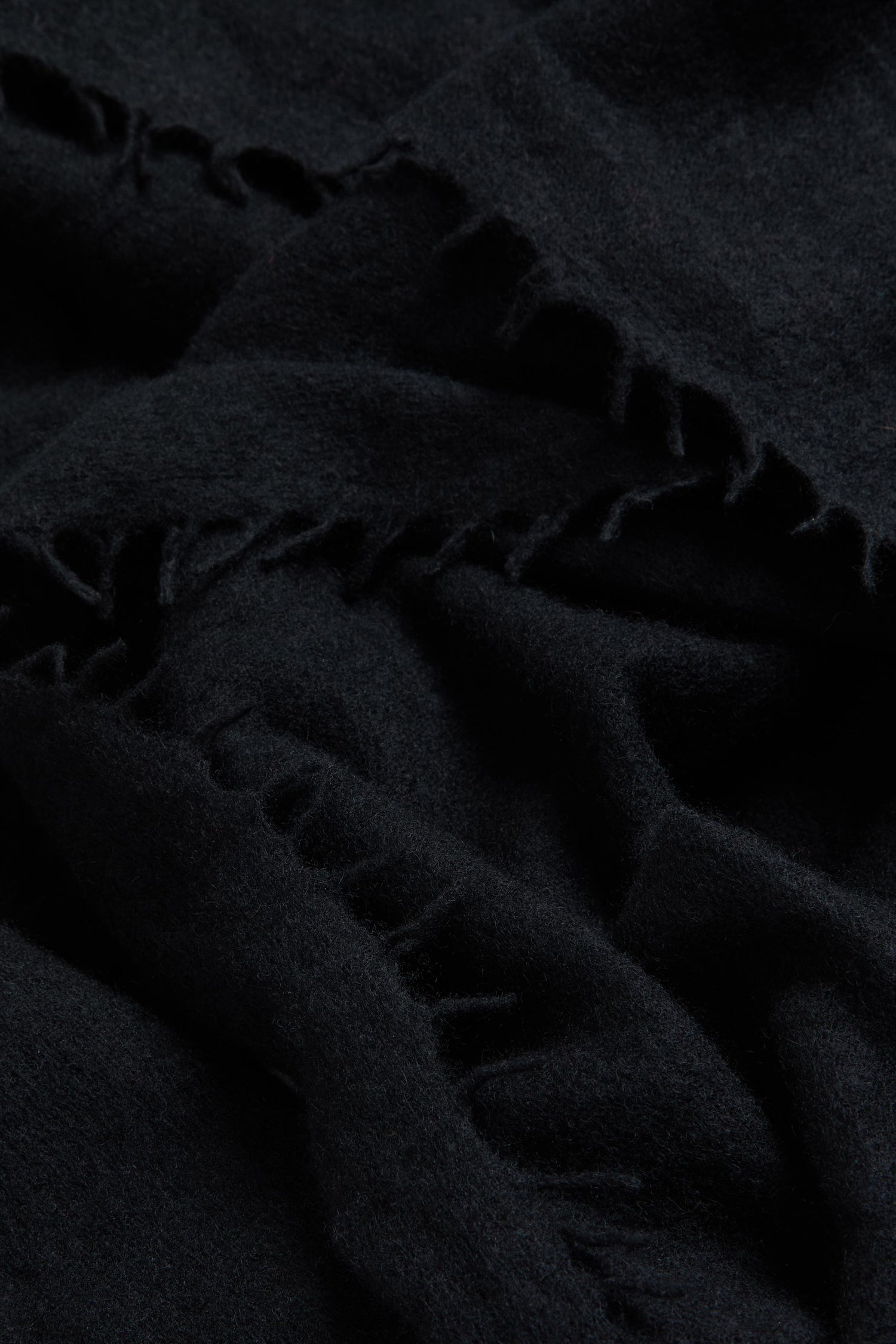 Close-up of the Black Soft Cashmere Scarf, highlighting its dark, luxurious fabric with visible stitching and frayed edges that showcase the soft woven cashmere texture and fine material details.