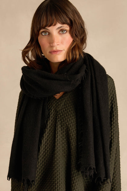 A woman with shoulder-length brown hair, dressed in a textured dark green top and wrapped in the Black Soft Cashmere Scarf, stands against a neutral background.