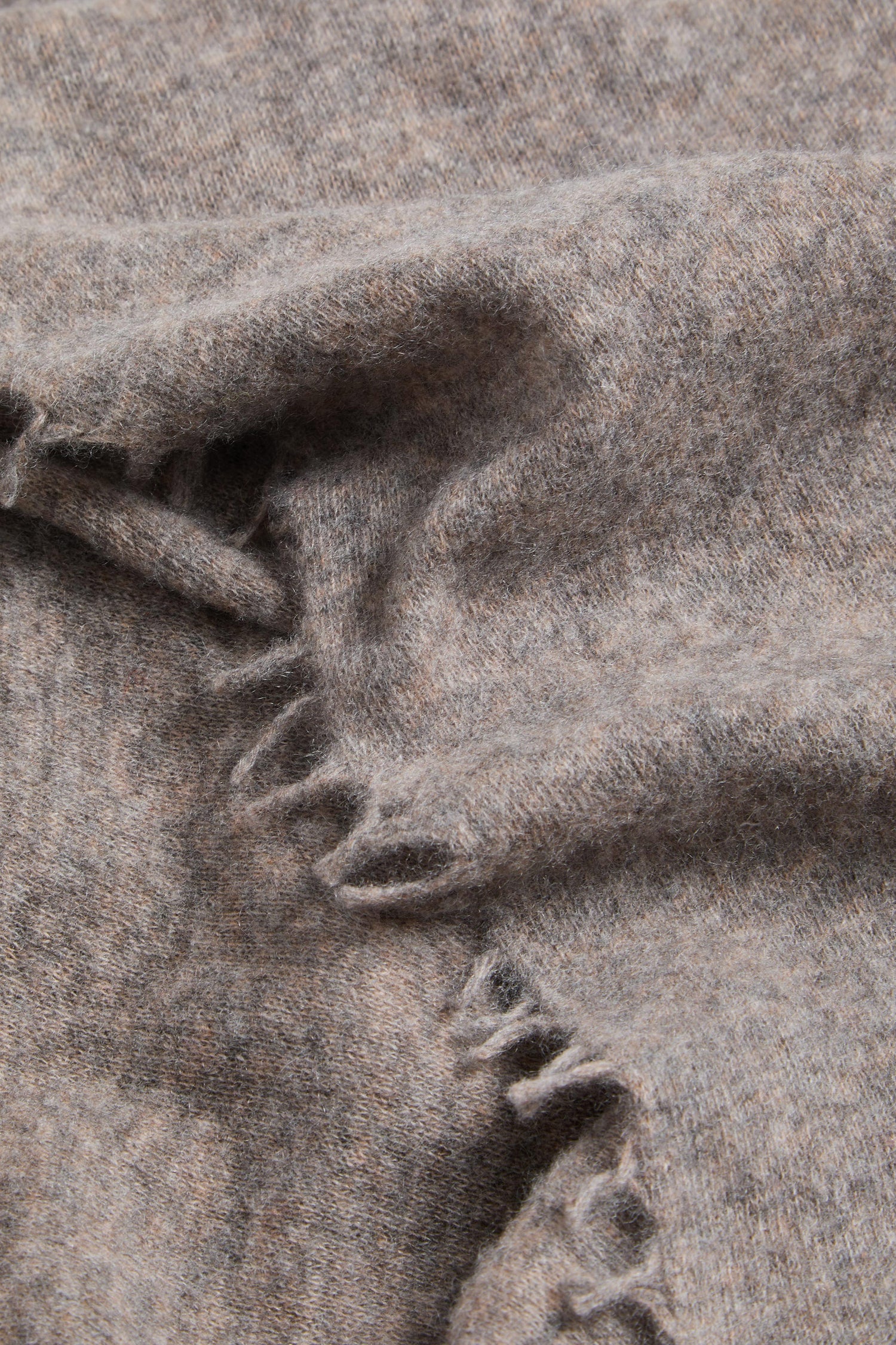 Close-up of the Sand Soft Cashmere Scarf, featuring a gentle fold and unfinished, frayed edges in a light brown hue.