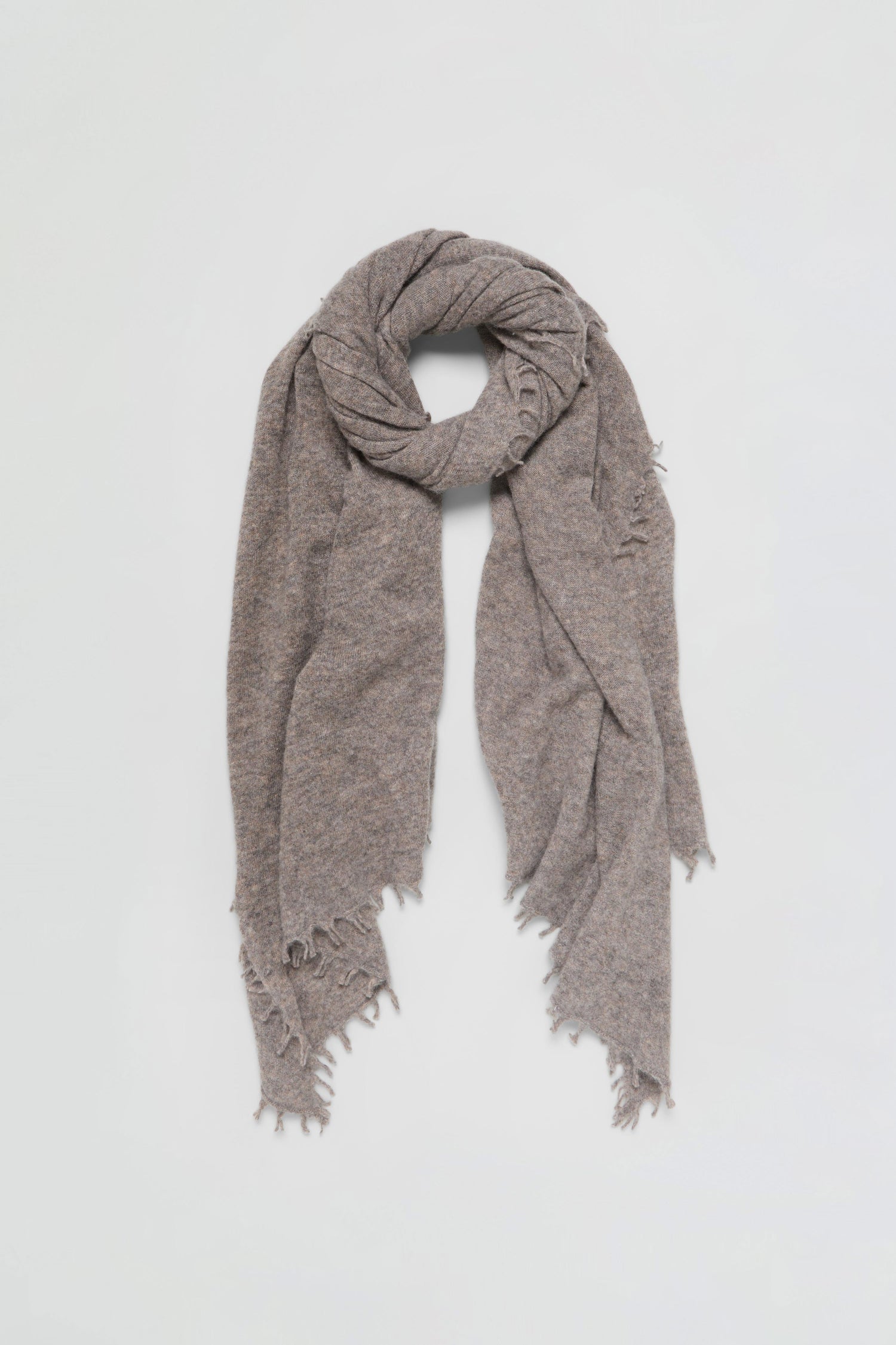 A Sand Soft Cashmere Scarf in light brown with frayed edges, loosely wrapped in a circular shape on a plain white background.