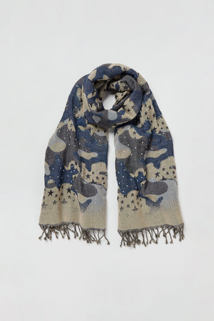 The Night Sky Sequin Wool Scarf, featuring a blue and beige camouflage pattern, star designs, sequin accents, small decorative studs, and fringed edges, is laid flat on a white background.