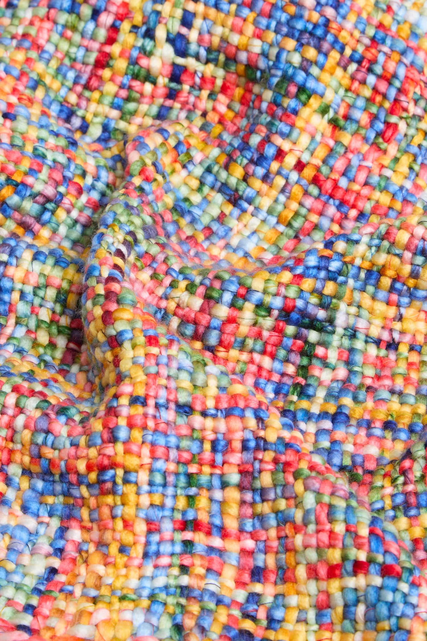 A close-up of the Rainbow Tassel Scarf highlights its colorful, textured woven fabric featuring a check pattern in blue, yellow, red, green, and pink threads, and showcases the soft brushed yarn that gives this scarf its lightweight warmth.