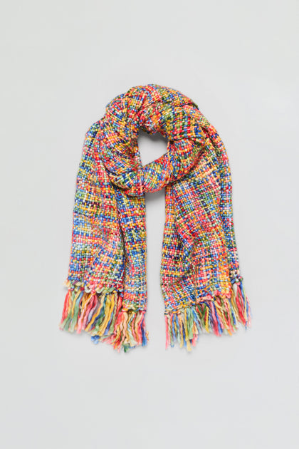 The Rainbow Tassel Scarf, made from soft brushed yarn for lightweight warmth, features multicolored woven design and fringed ends, showcased against a plain light background.