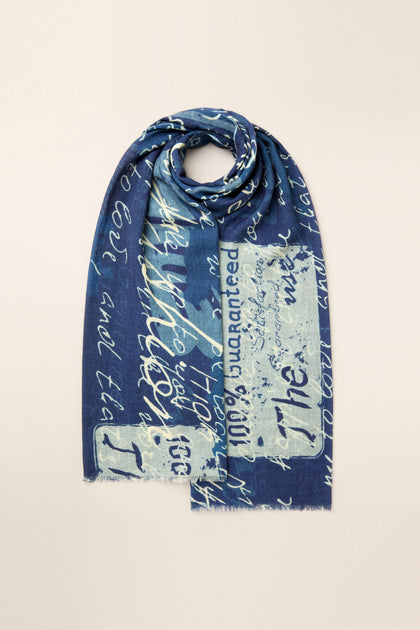 The Love Language Printed Scarf, adorned with white cursive text and faded rectangle patterns against a blue backdrop, is neatly folded against a plain background, showcasing its vintage-inspired design reminiscent of love letter prints.