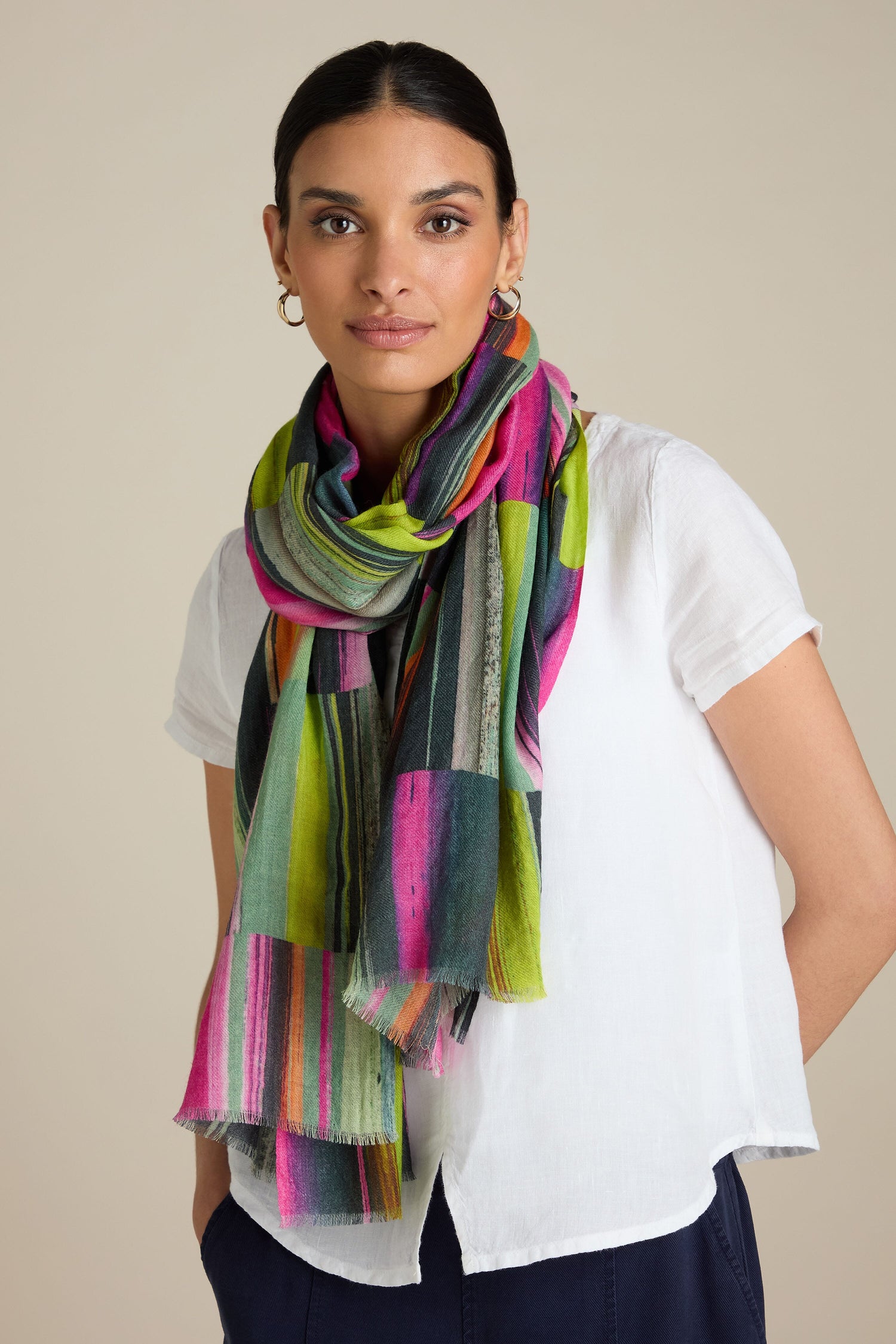 A person with tied-back hair wears a white shirt and a Block Print Wool Mix Scarf featuring colorful stripes and block-print motifs.