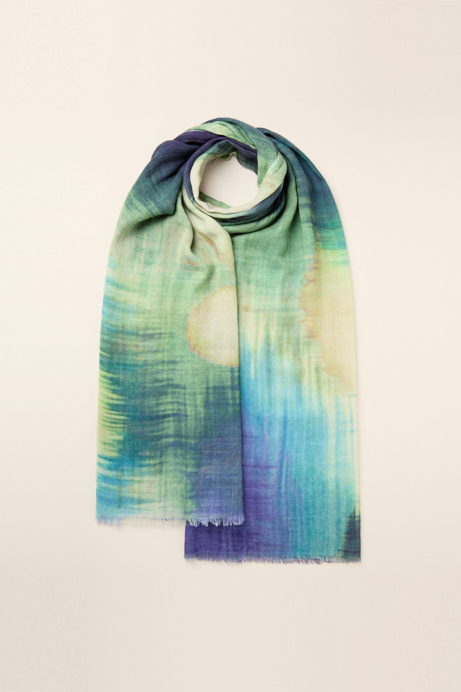 An exquisite rectangular scarf showcasing a watercolour-inspired gradient pattern in captivating shades of blue, green, and beige, draped gracefully against a light background. The Colour Blend Circle Print Scarf is crafted from sumptuously soft fabric for an elegant touch.