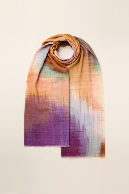 The Colour Blend Circle Print Scarf features a watercolor-inspired design with an abstract pattern in vibrant shades of orange, purple, green, and blue, laid flat with one end rolled.