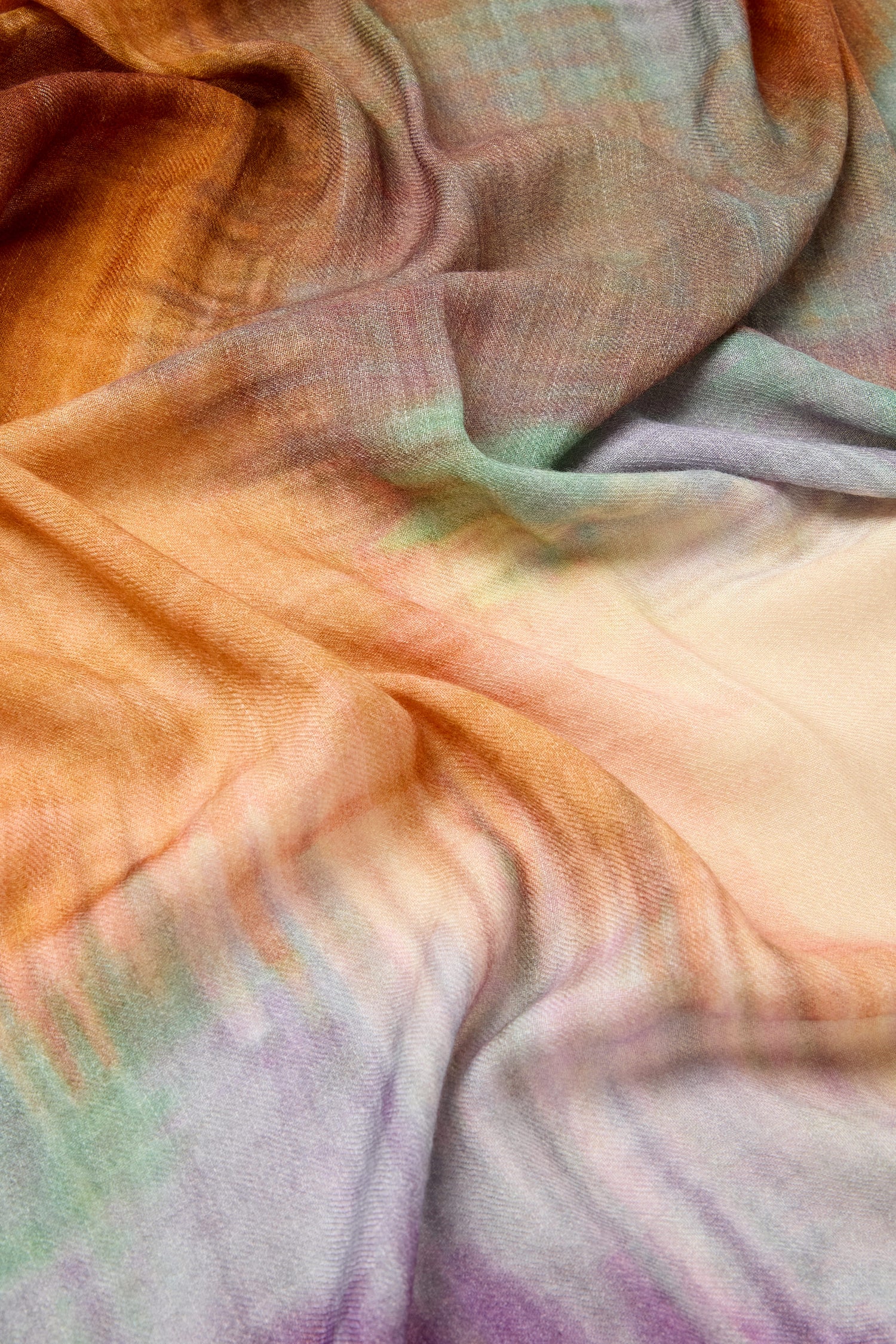 The Colour Blend Circle Print Scarf showcases a sumptuous, soft fabric with shades of orange, green, and purple. It features a subtle, mottled pattern reminiscent of a watercolor-inspired design.