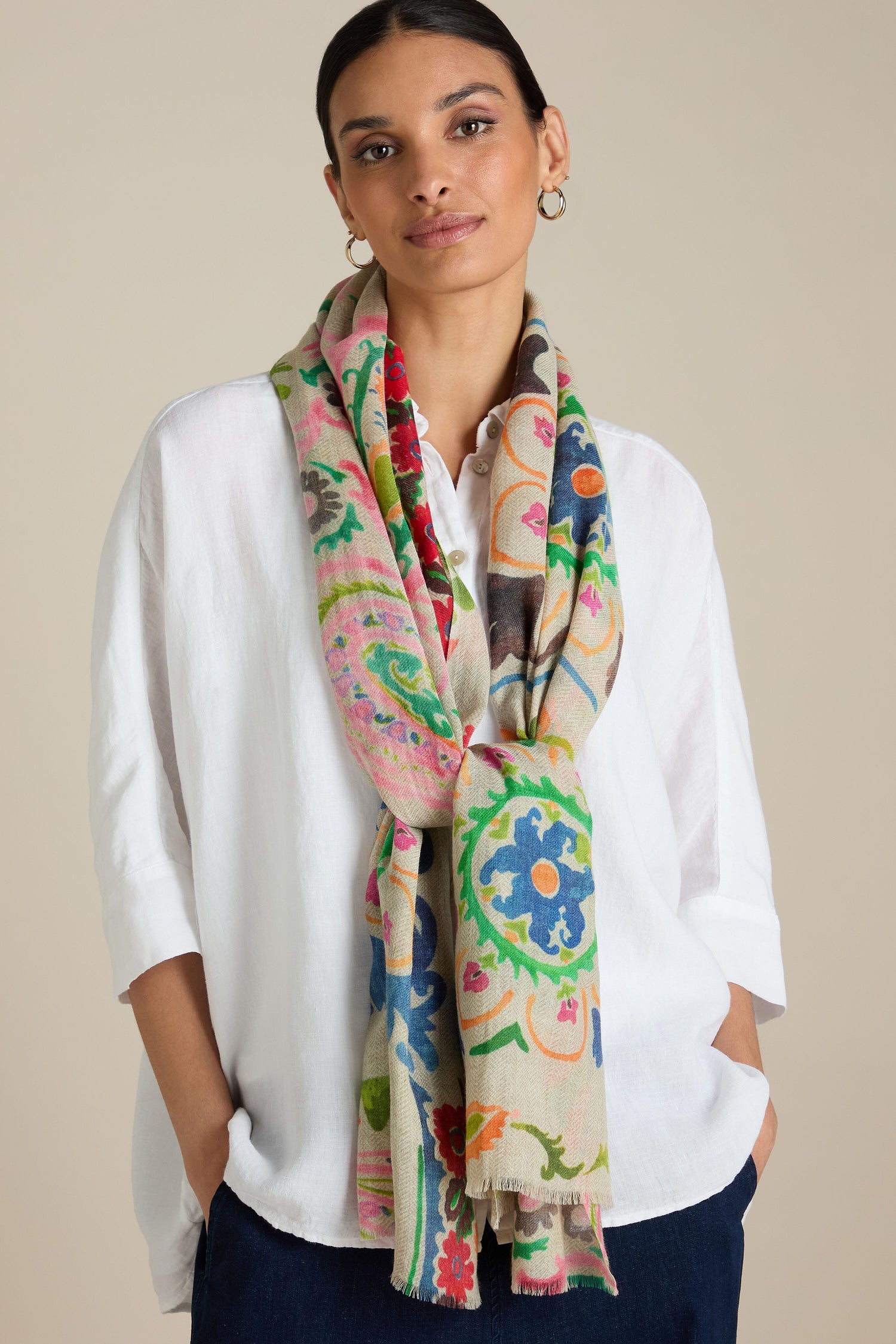 A person wearing a white shirt and the Painted Paisley Wool Mix Scarf, featuring an intricate hand-painted floral design, stands against a plain background. This versatile accessory adds a vibrant touch to any outfit for all-occasion styling.