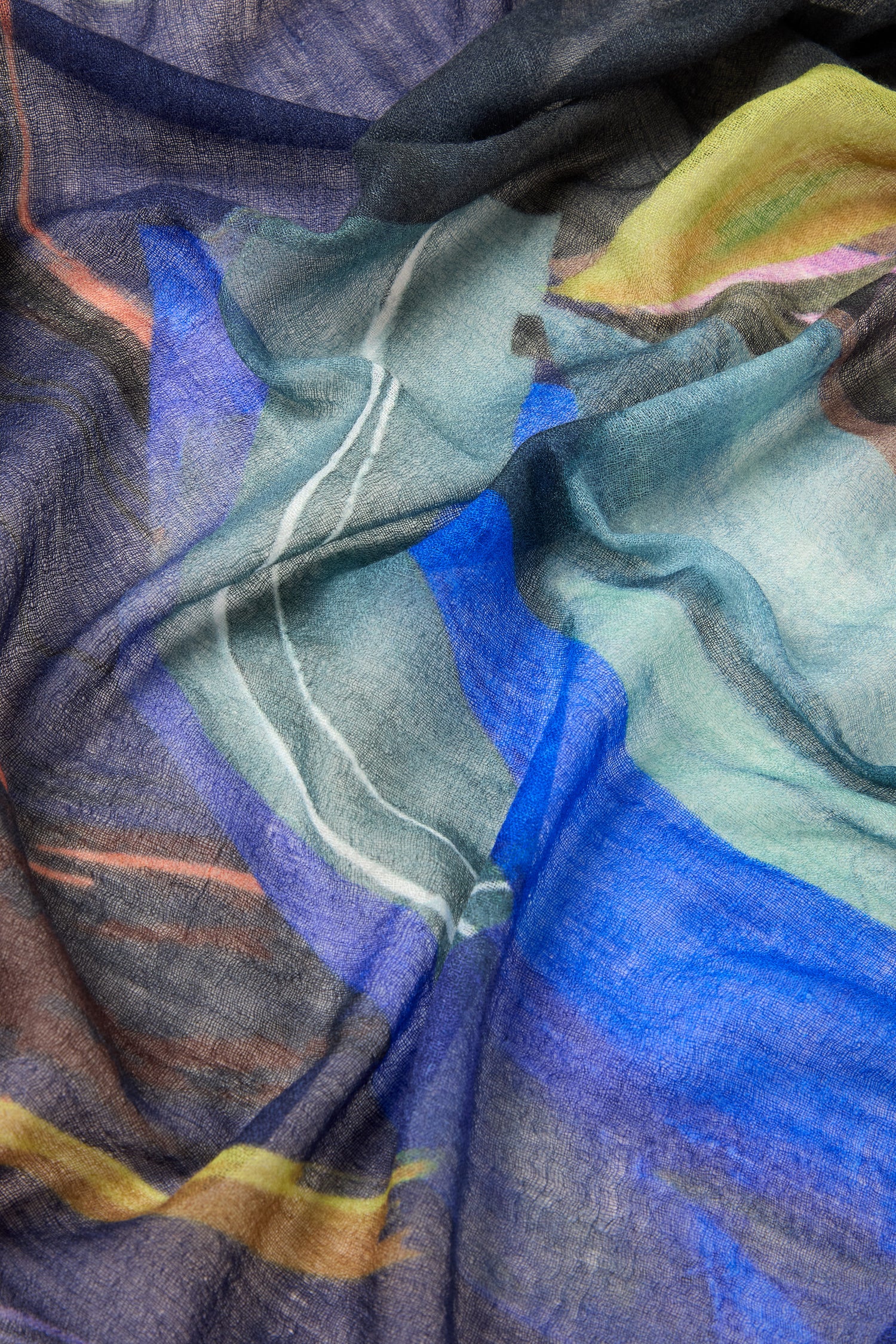 A close-up image of the Abstract Plume Wool Scarf, showcasing its premium wool fabric adorned with abstract patterns in shades of blue, green, yellow, and black. The wavy lines and soft textures combined with the hand-painted design create a unique and artistic look.