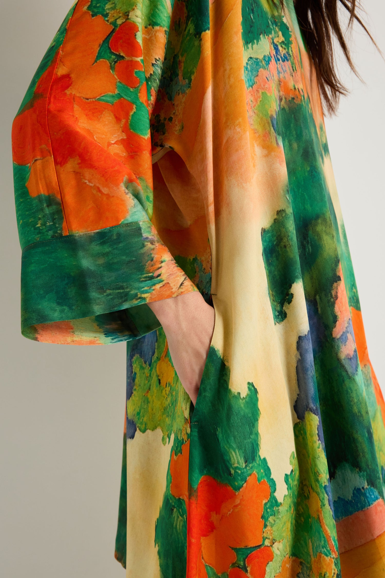 A person is shown from shoulder to thigh wearing the Japanese Garden Boxy Tunic, an oversized woven viscose piece with vibrant orange, green, yellow, and blue abstract patterns.