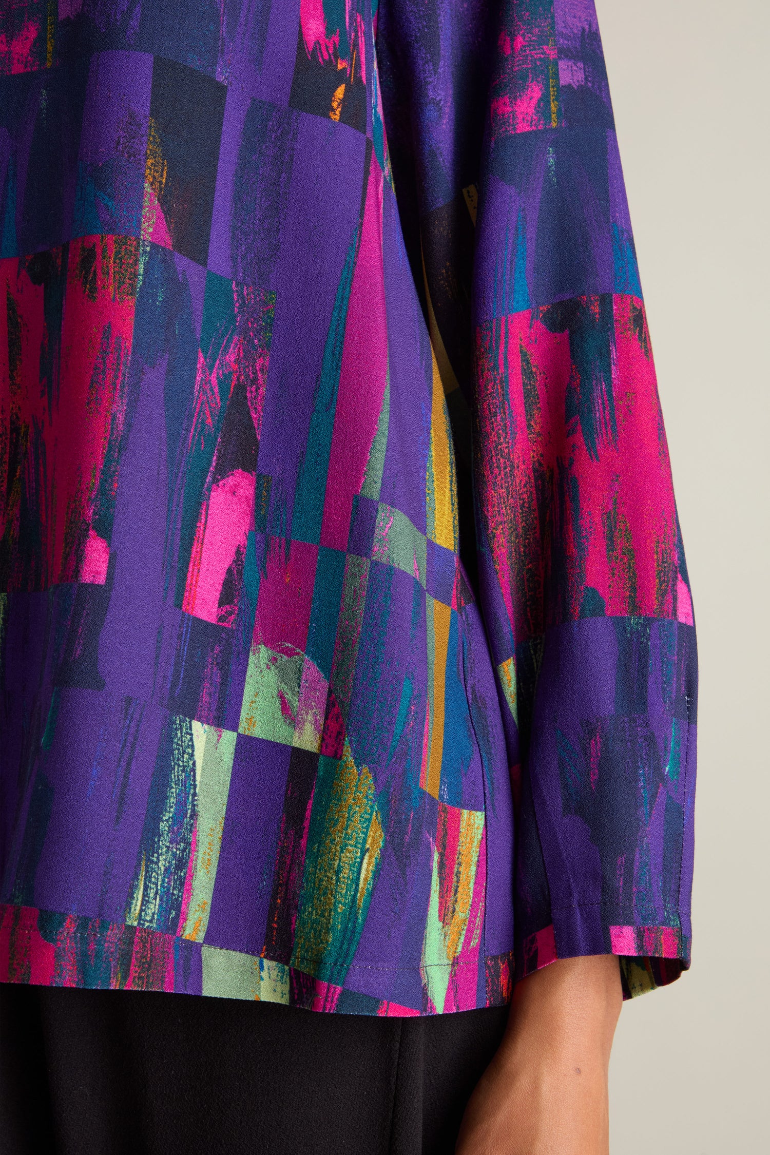 Close-up of a multicolored, abstract-patterned sleeve against a neutral background, showcasing the vibrant jewel tones of purple, pink, teal, and yellow. This striking design is an exquisite example of Aino fashion and is beautifully embodied in the Aliza Block Print Top.