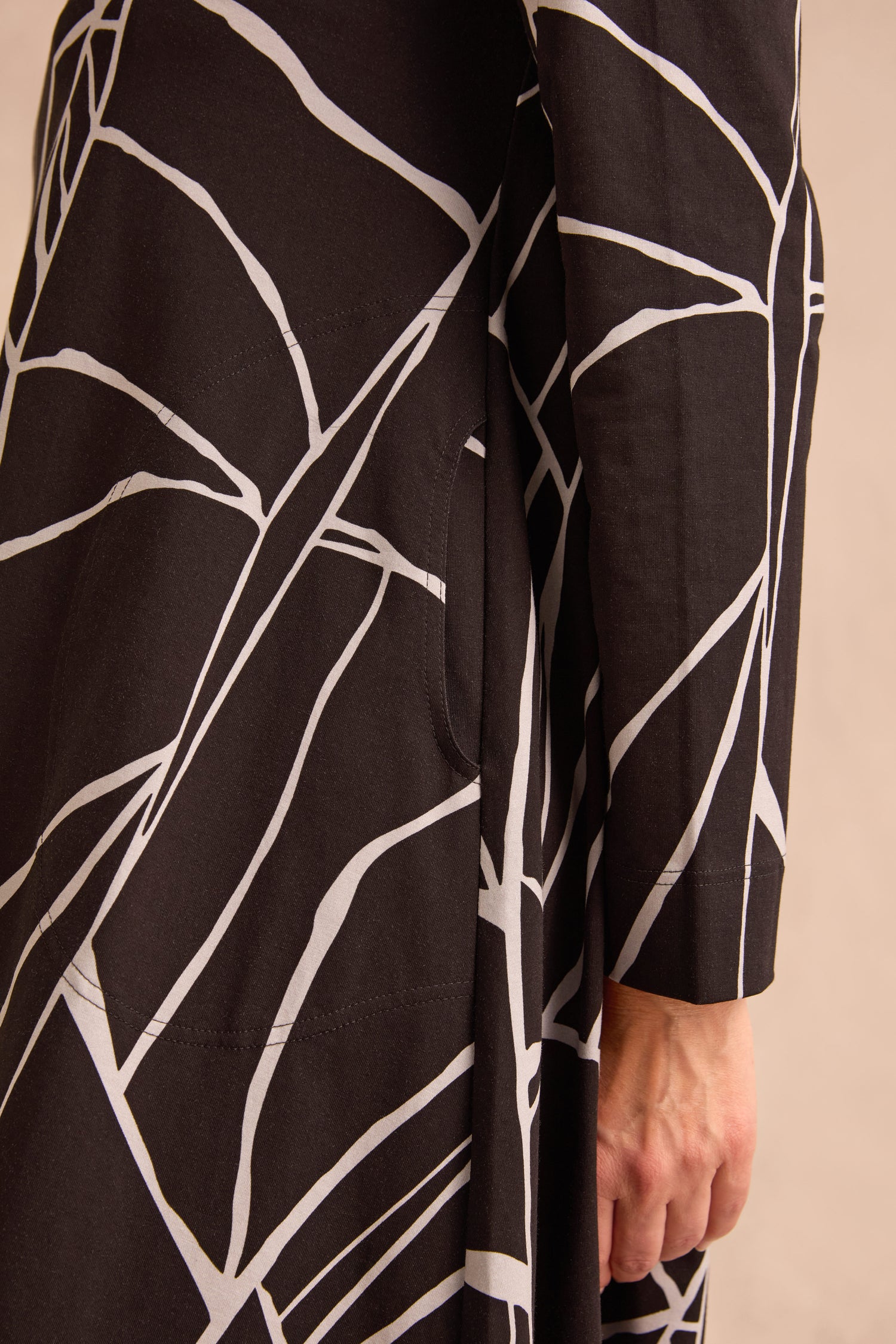 Close-up of a person’s hand resting against the Linear Print Jersey Flared Dress, which features bold white abstract line patterns on black fabric.