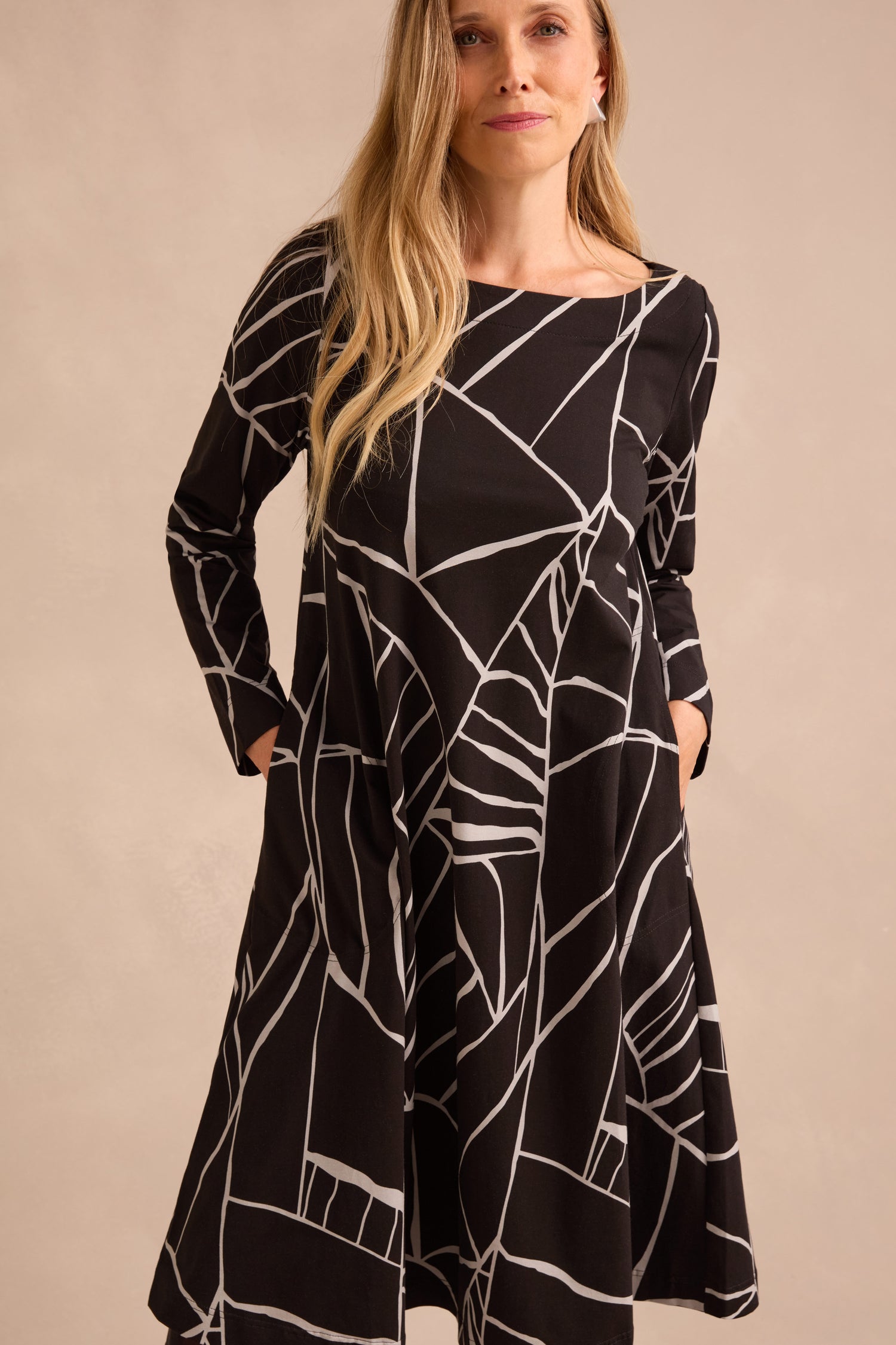 A woman wearing the Linear Print Jersey Flared Dress, featuring long sleeves and a bold black-and-white abstract geometric design, stands against a neutral backdrop.