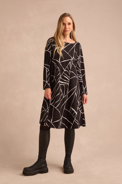 A woman stands against a neutral background wearing the Linear Print Jersey Flared Dress, styled with black leggings and boots.
