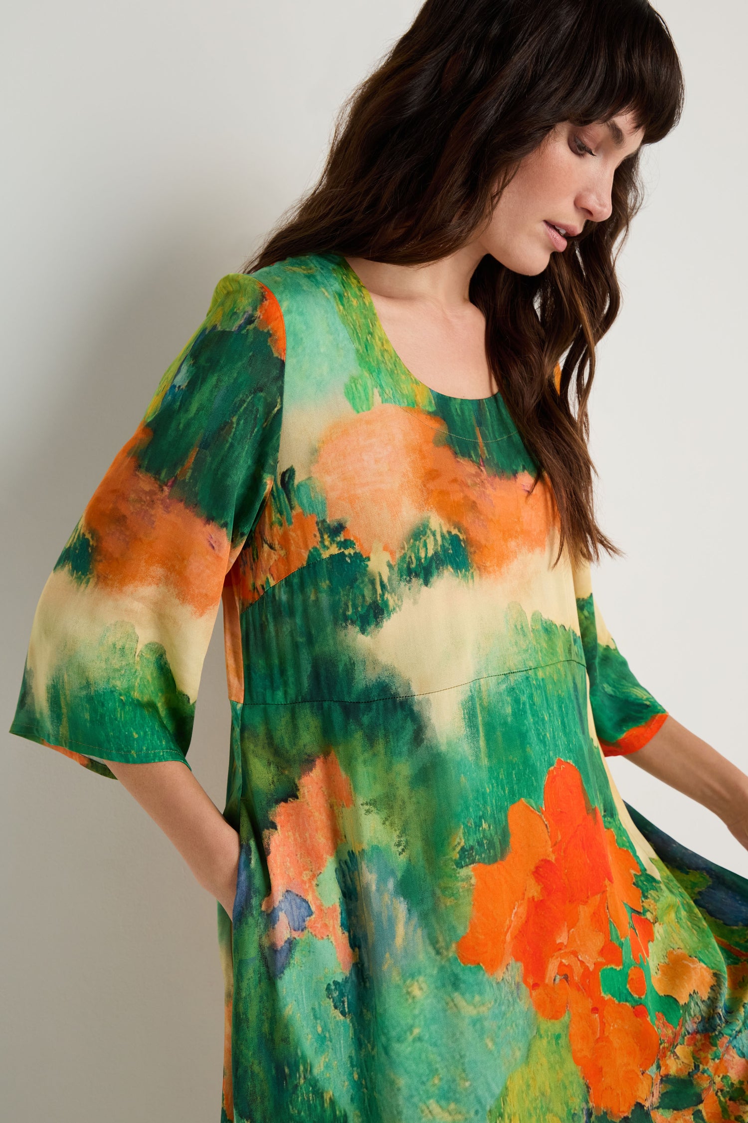 A woman stands against a plain light background wearing the Japanese Garden Flared Dress, featuring a colorful abstract pattern in green, orange, yellow, and blue on breathable woven viscose.