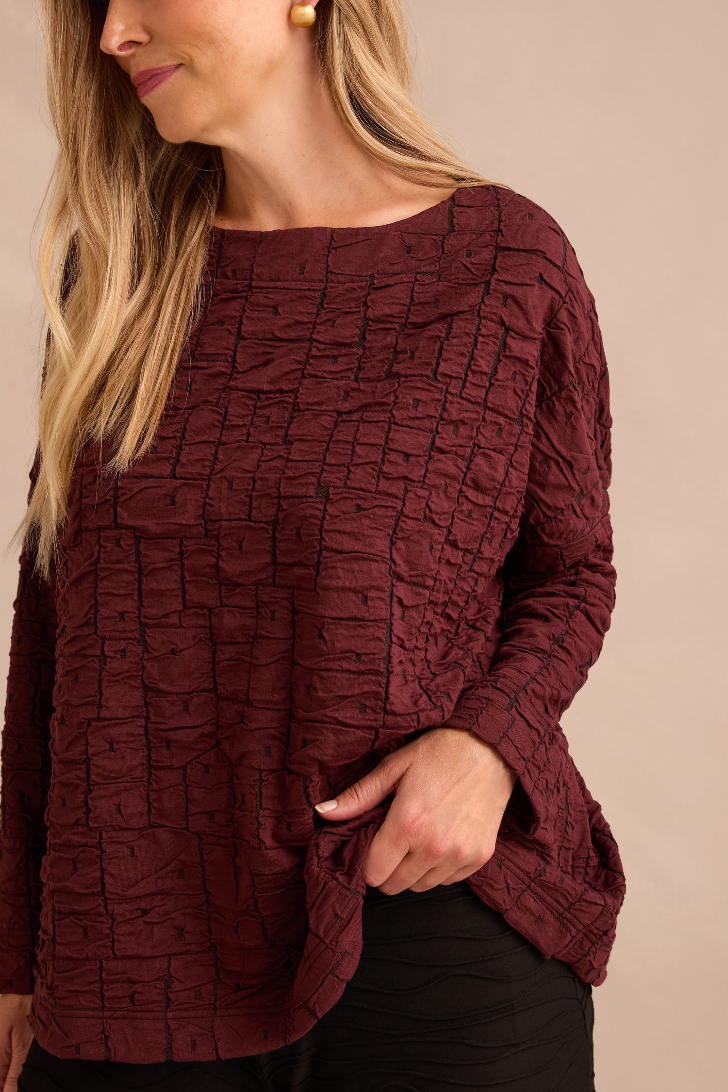 A woman wears the Bordeaux Textured Squares Jersey Boxy Top, featuring a subtle square pattern in maroon, paired with black pants and standing against a neutral background.