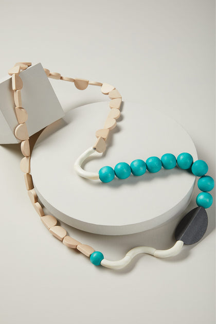 A Squiggle Shapes Necklace on a circular display stand with a light-beige geometric bracelet.