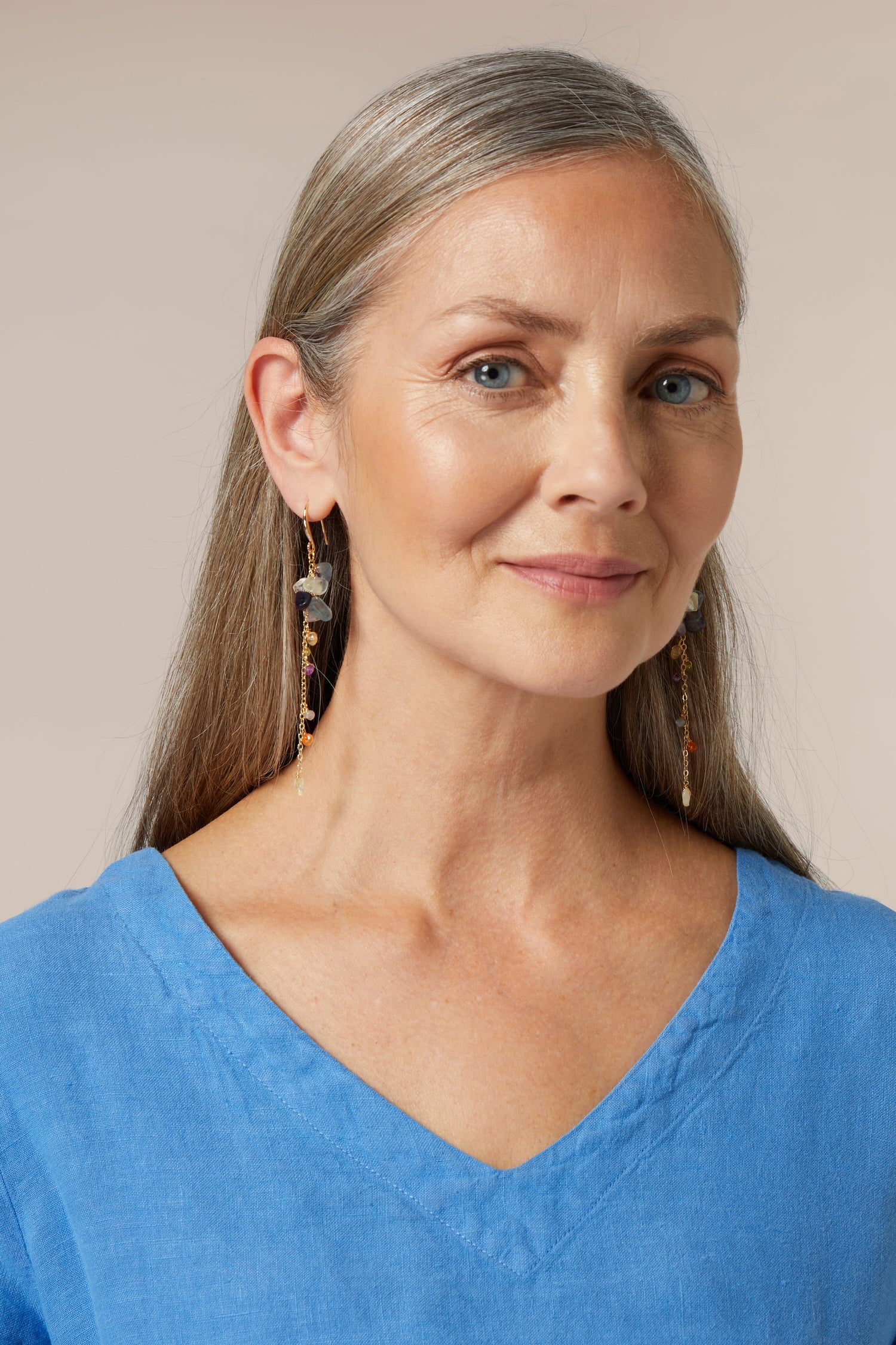 Sentence with product name: Portrait of a mature woman with grey hair wearing a blue top and Mini Stones Earrings.