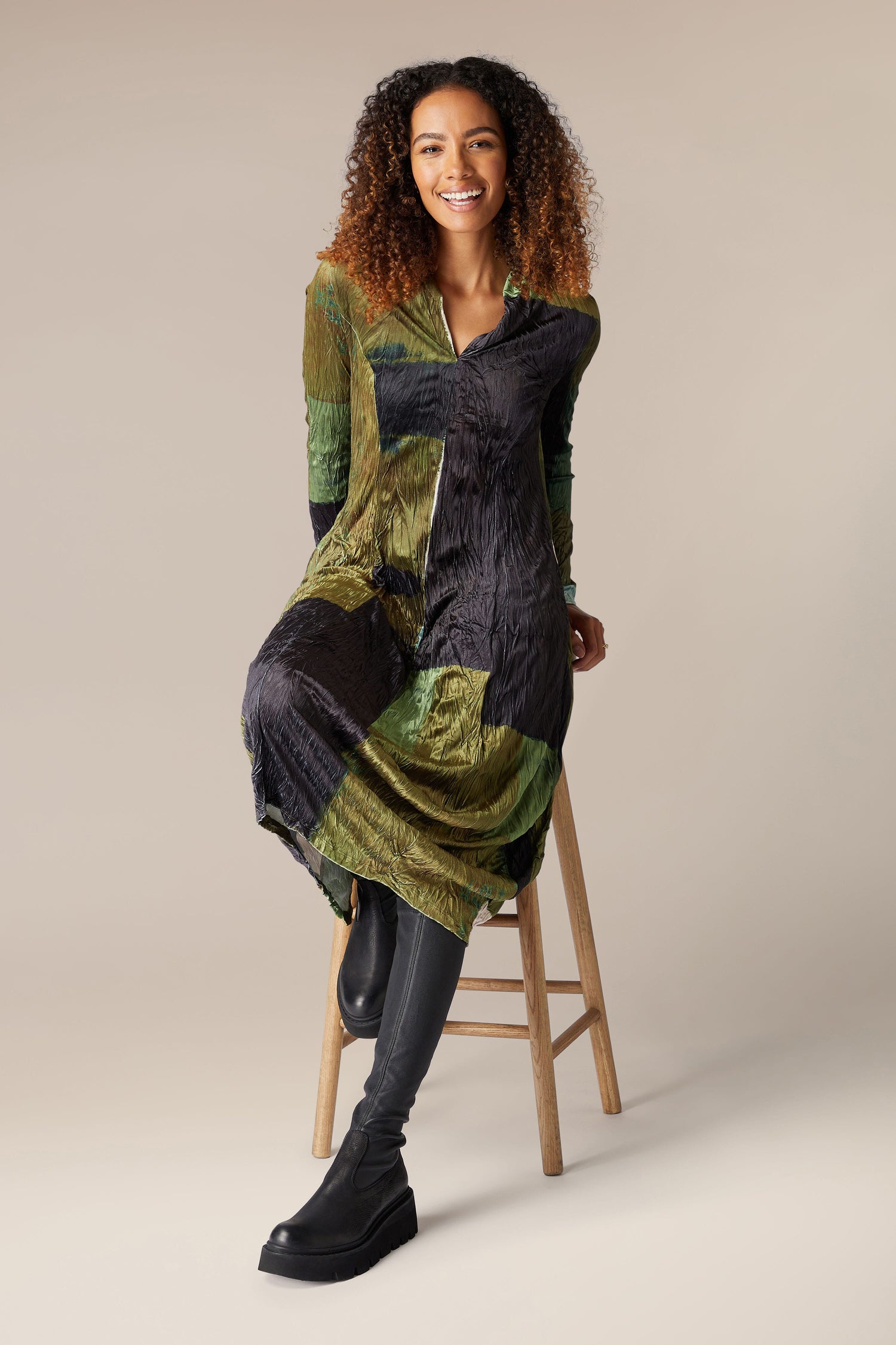 A woman is sitting on a stool in a Block Velvet Dress featuring long sleeves.
