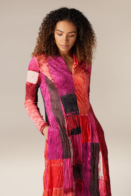 A woman wearing a long-sleeved Block Velvet Dress in pink and red.