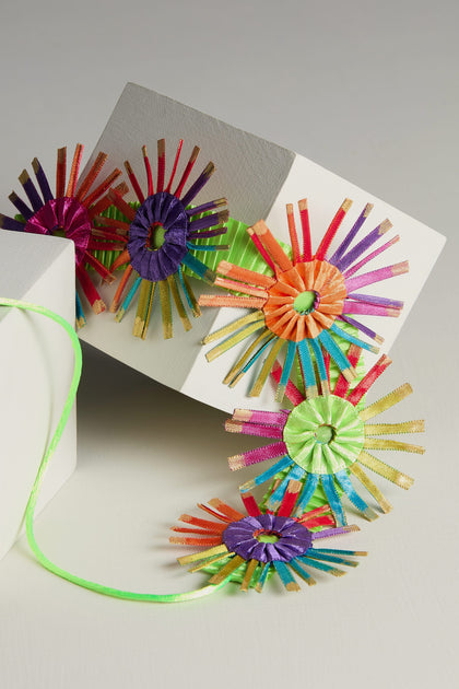 A lightweight fabric construction of a Rainbow Bloom Pleated Necklace on top of a card.