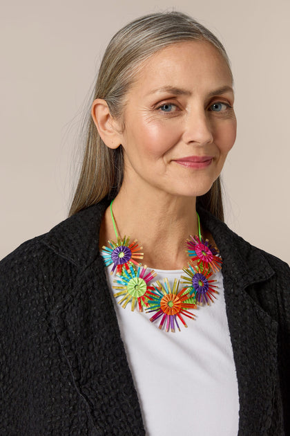 A woman wearing the Rainbow Bloom Pleated Necklace, a sculptural piece with colorful lightweight fabric construction.