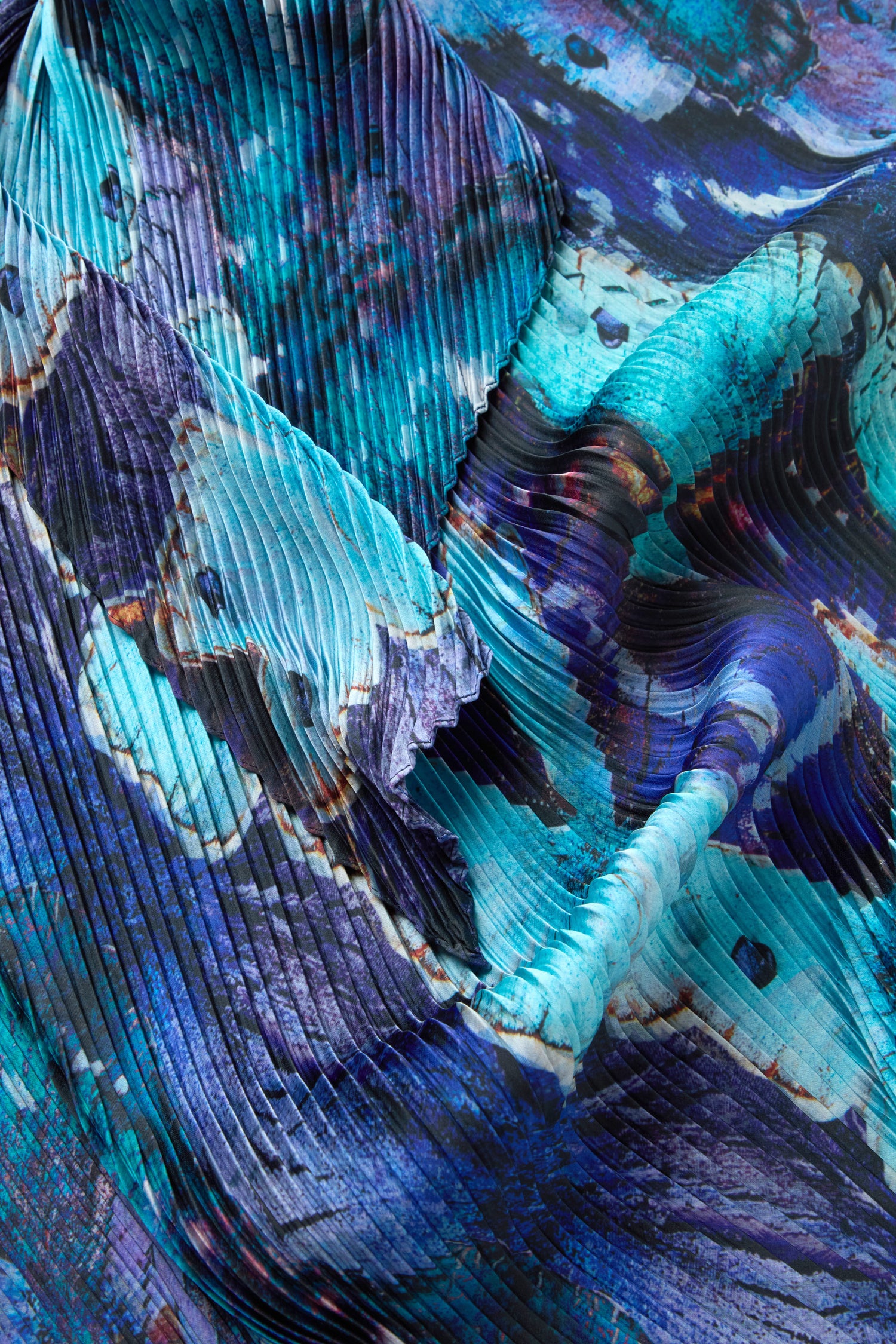 Close-up of the Butterfly Pleat Scarf, a lightweight satin accessory featuring blue, purple, and turquoise abstract watercolor-inspired patterns and dramatic pleats—perfect for making a statement with any outfit.
