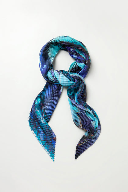 The Butterfly Pleat Scarf in blue features a pleated satin design on a white background, making it a perfect lightweight statement accessory.