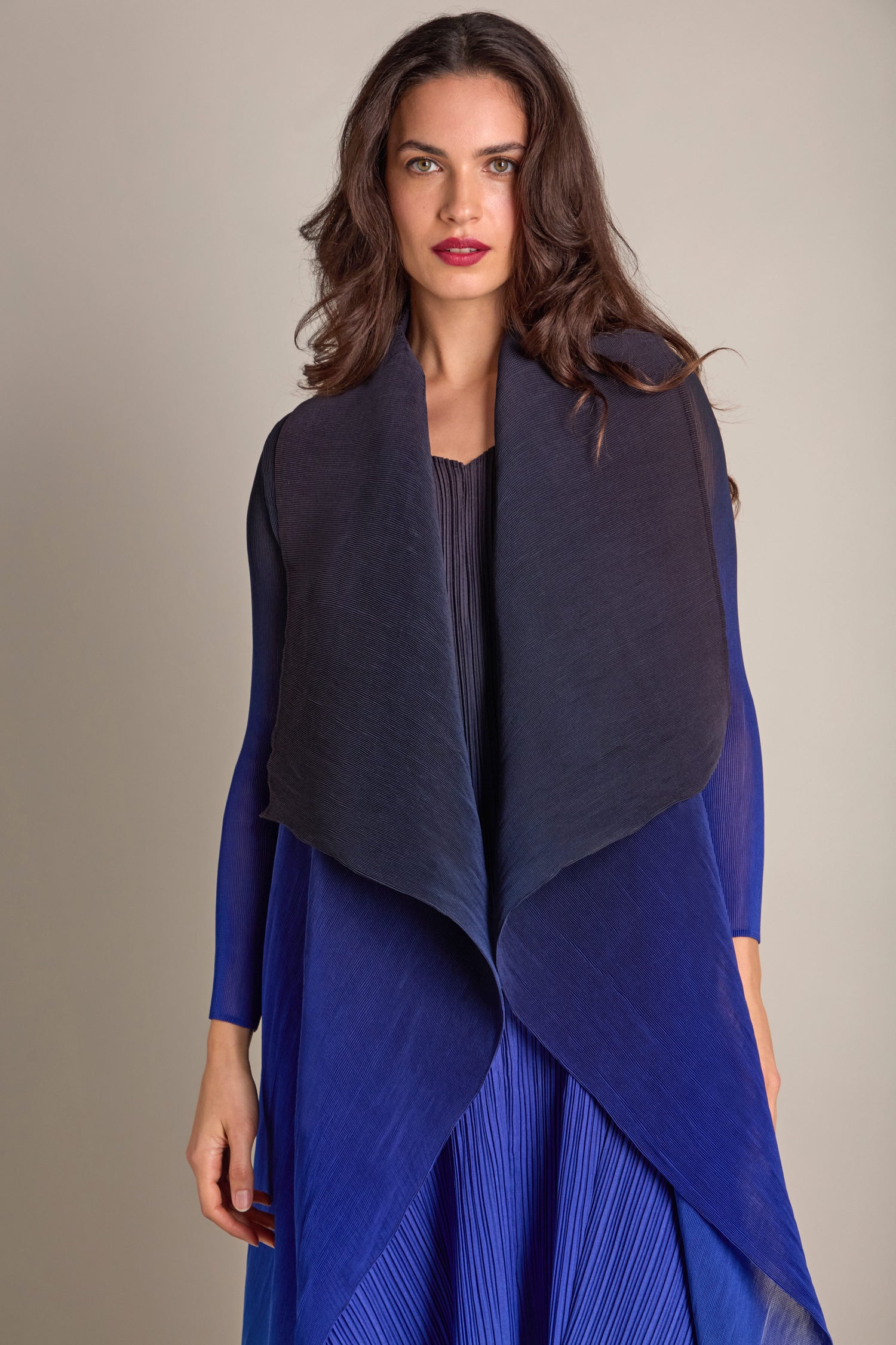 A person wearing a Pleated Jacket and a dark shawl stands against a plain background, with the lightweight layer adding elegance to their ensemble.