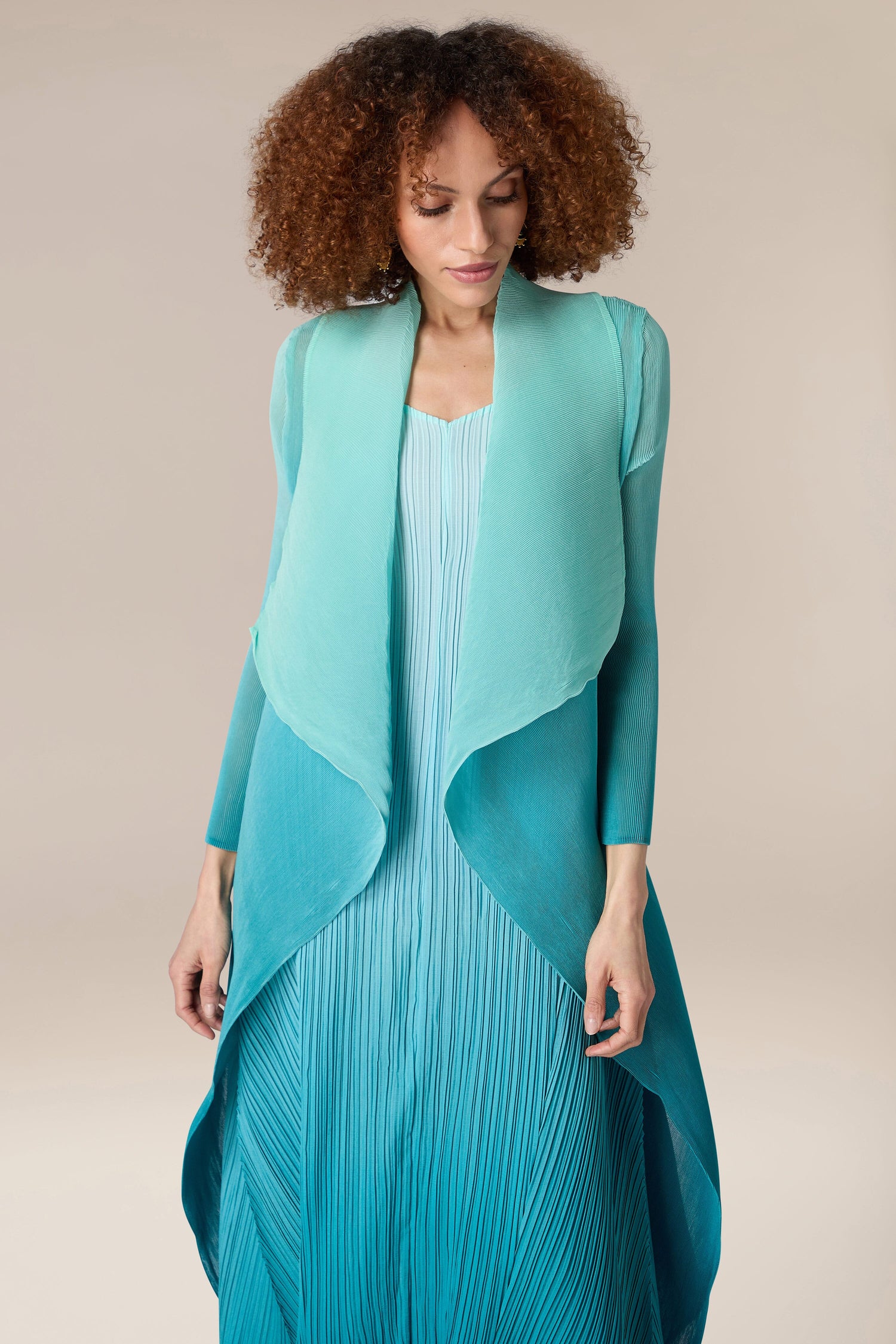 A woman styled in an Alquema teal dress paired with a Pleated Jacket.