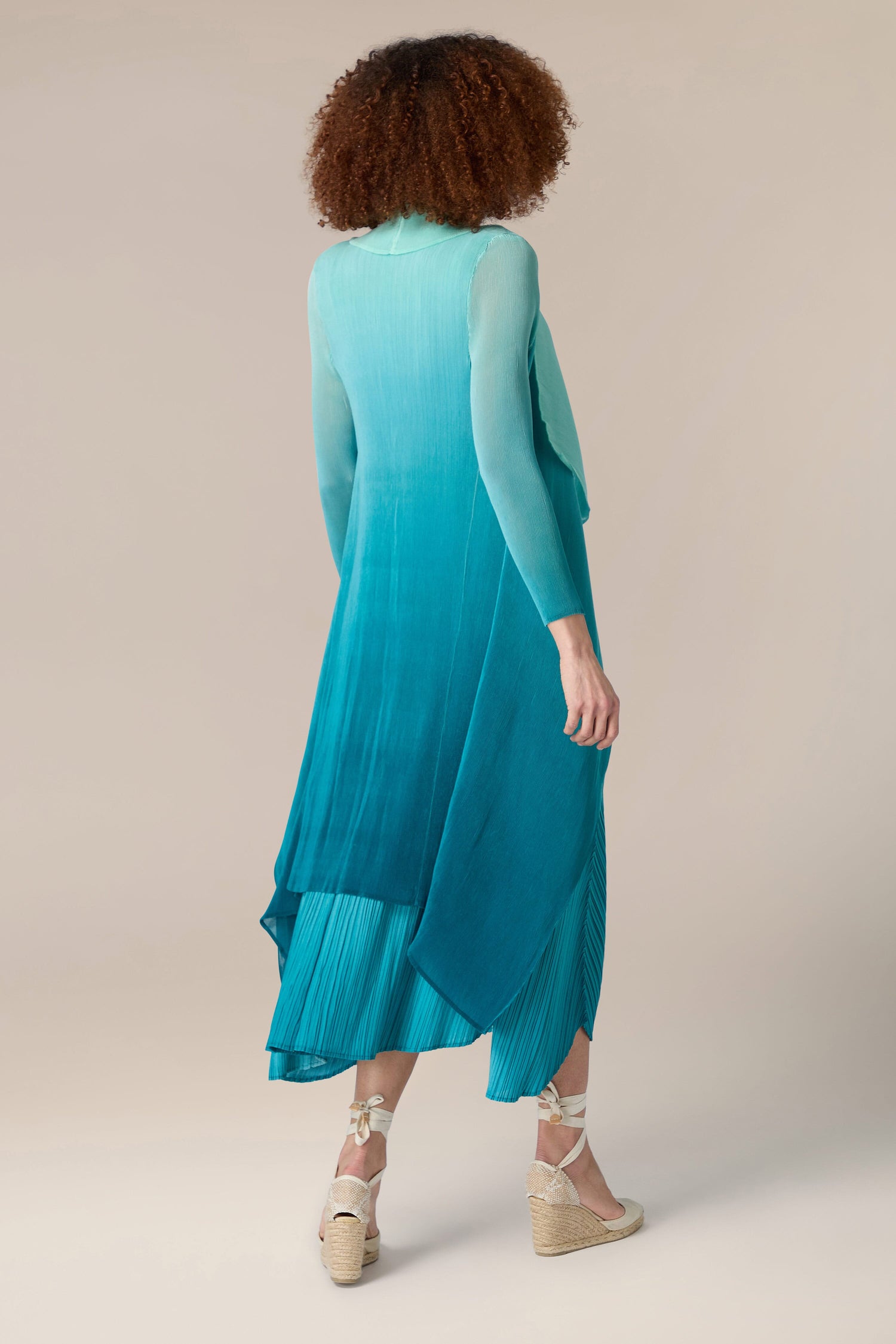 A woman wearing a teal ombre pleated jacket in Alquema style.
