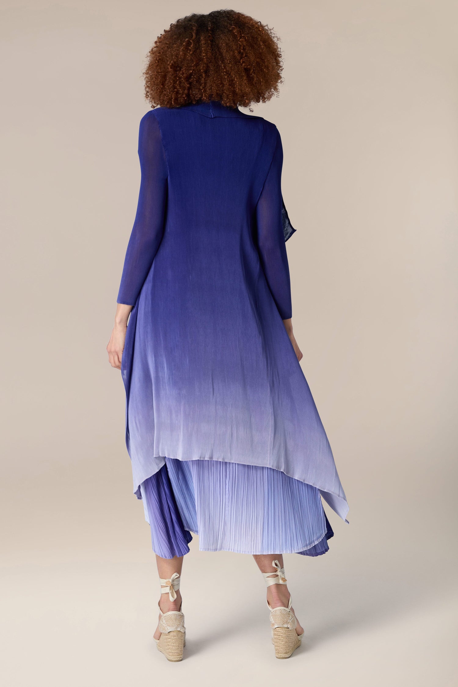 The woman is seen from behind wearing a blue ombre Pleated Jacket.