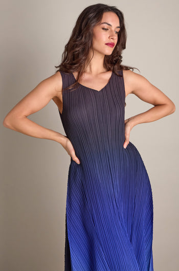 A person stands confidently in a Pleated Dress, its detailed pleated fabric forming an elegant gradient from black to blue, hands resting on their hips.