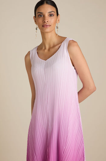 A woman is wearing a sleeveless, pink and white gradient Pleated Dress with a relaxed silhouette. She has her hair pulled back and is accessorizing with dangling earrings, adding a touch of bohemian flair to her ensemble.