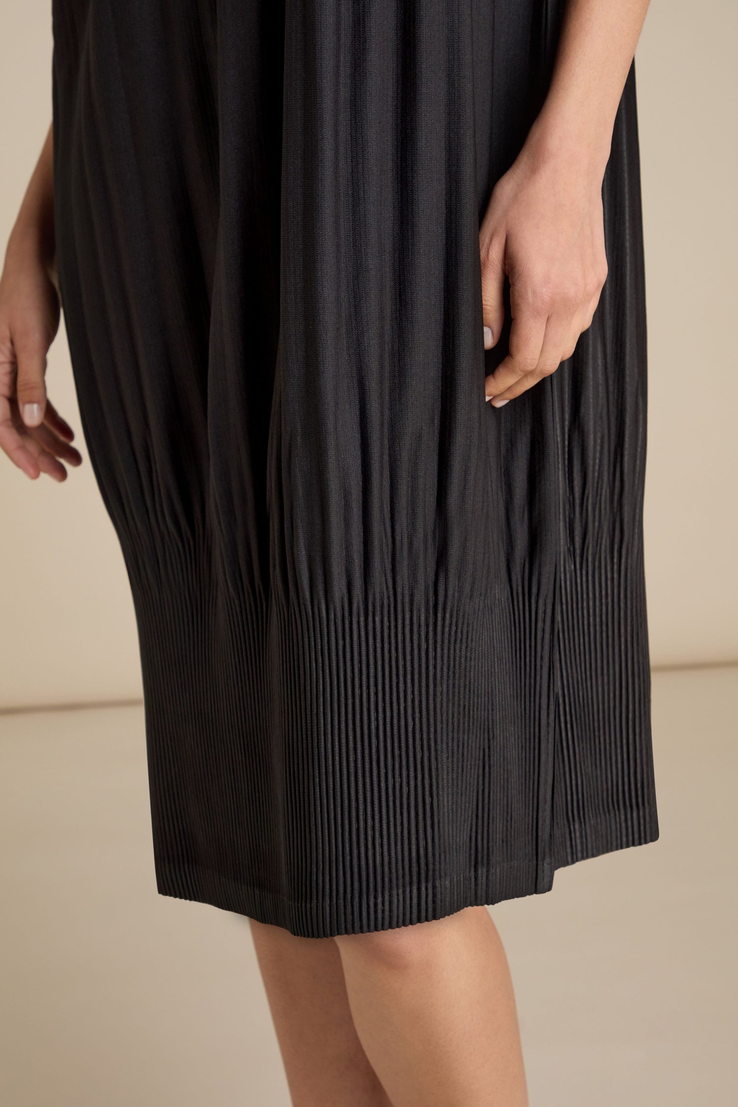 Close-up of a person wearing an Alquema Pleated Babydoll Dress in black. The person's hand is visible, resting along the side of the dress, paired perfectly with statement necklaces.