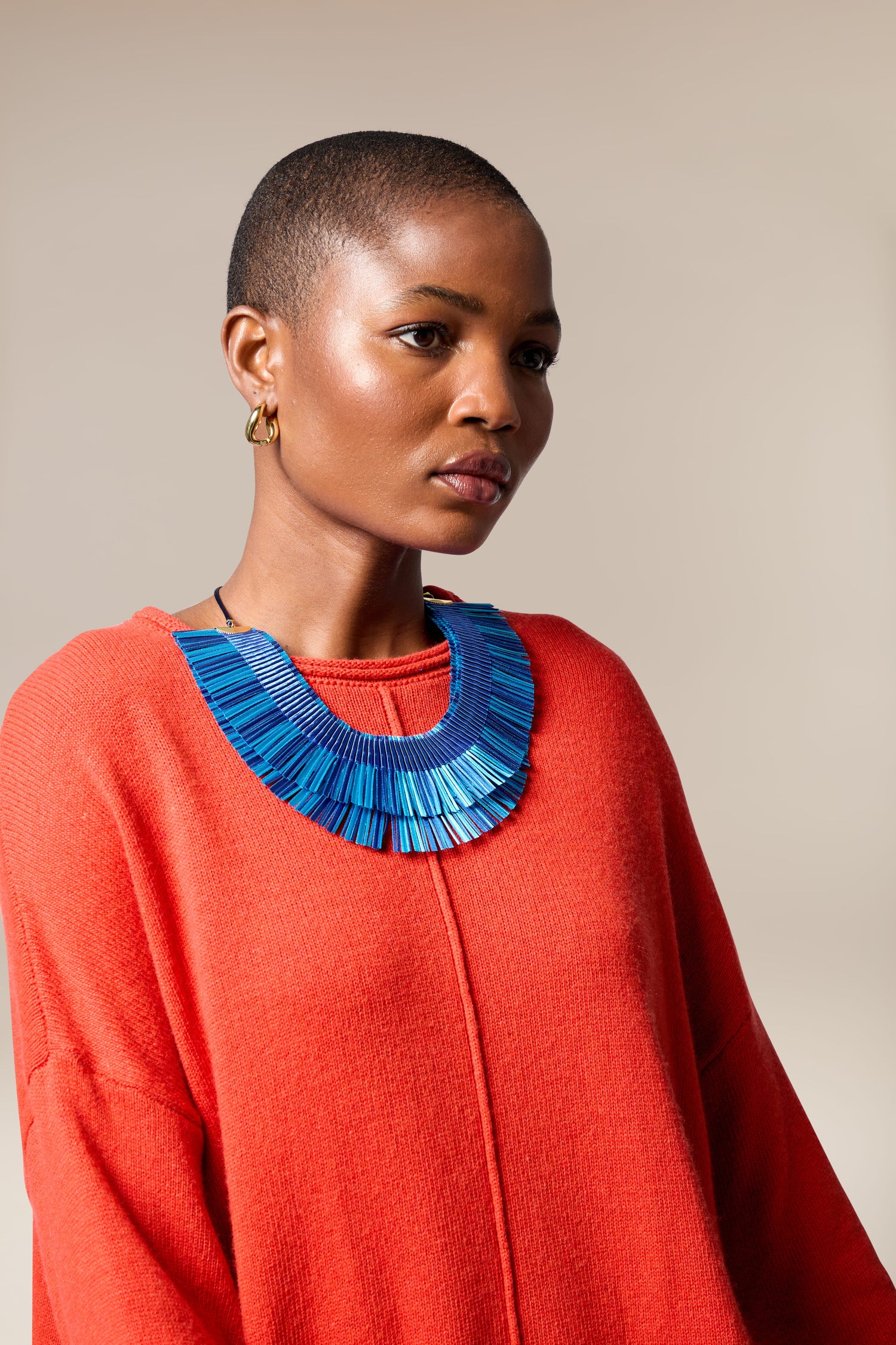 A person with short hair wears a bright red sweater and a bold blue Double Fringe Necklace, posing against a neutral background.