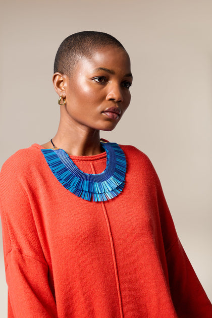 A person with short hair wears a bright red sweater and a bold blue Double Fringe Necklace, posing against a neutral background.