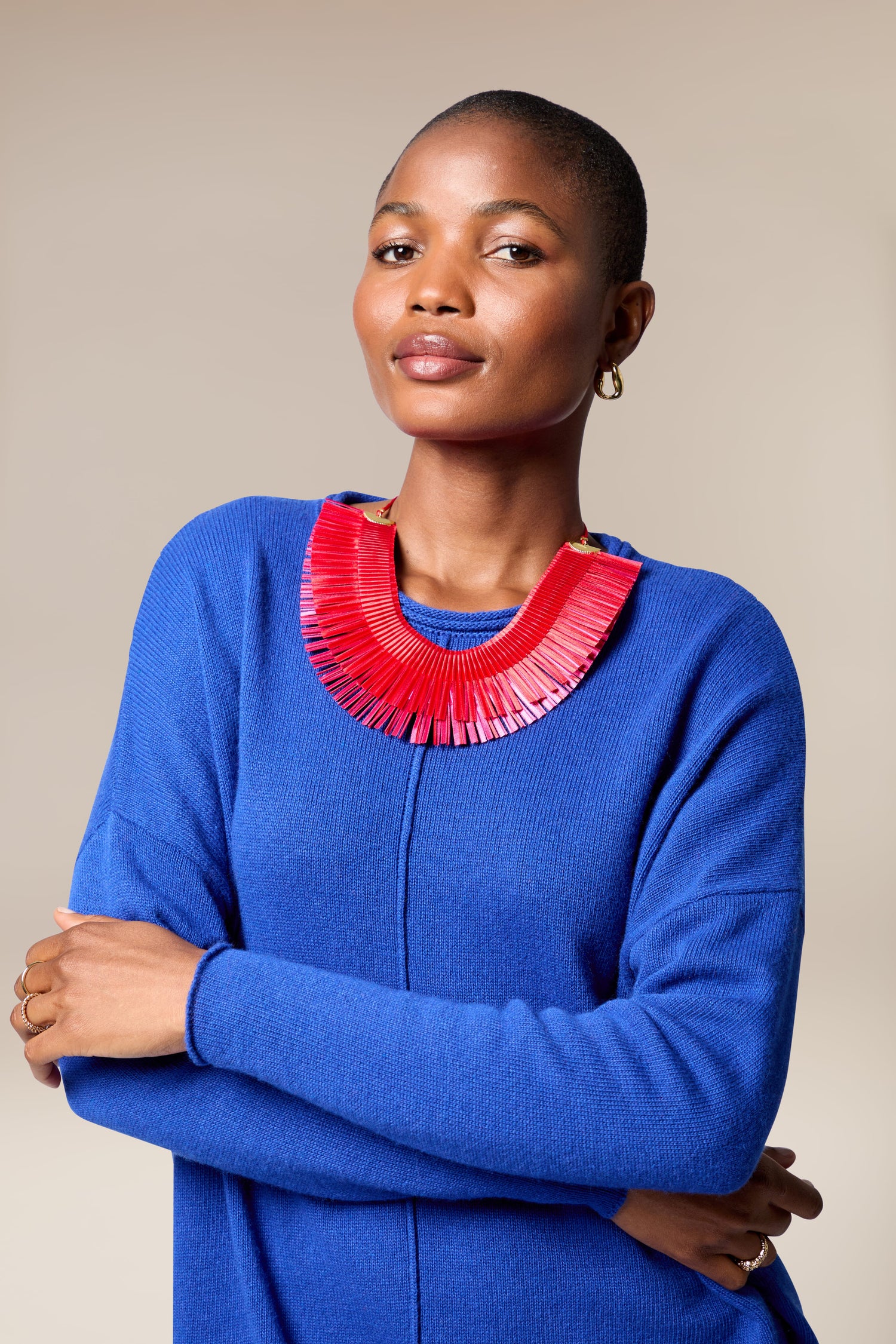 A person stands confidently with arms crossed, wearing a blue sweater and the Double Fringe Necklace, against a neutral background.