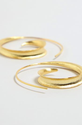 The Gold Vermeil Swirl Earrings rest on a light surface, showcasing sculptural spiral hoops with a modern, elegant design.