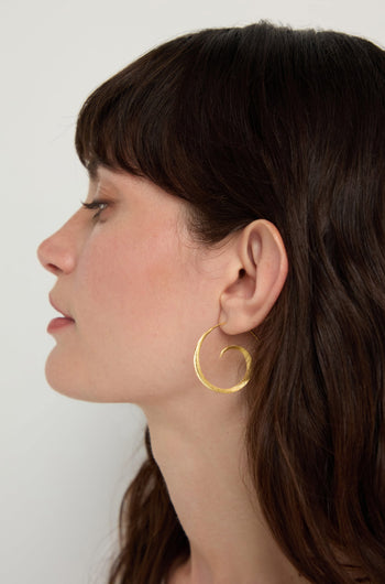 A woman with long brown hair is shown in profile wearing Gold Vermeil Swirl Earrings.