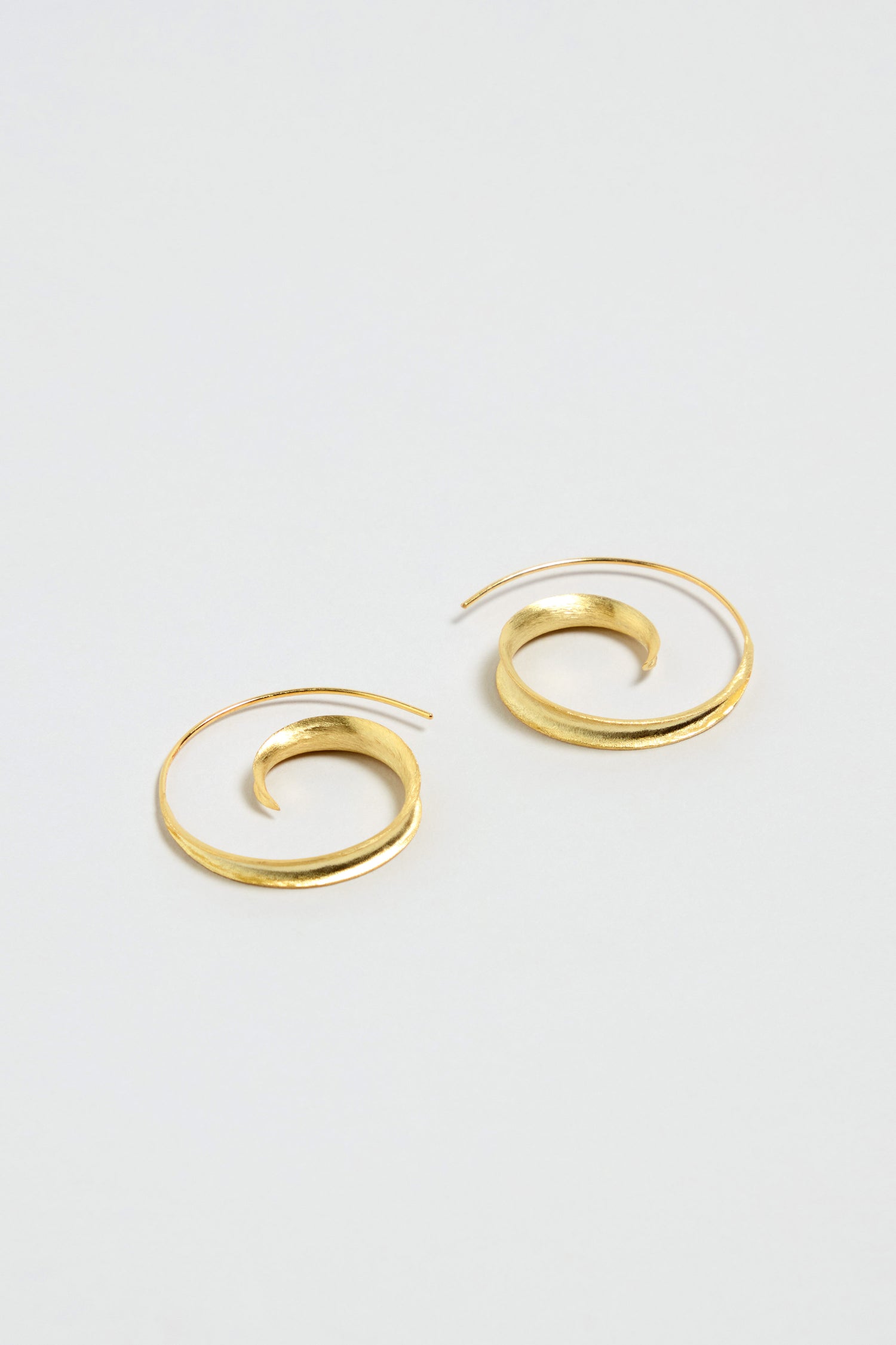 The Gold Vermeil Swirl Earrings are displayed on a plain, light-colored background, showcasing their sculptural design.