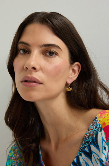 A woman with long brown hair wears a colorful patterned top and Gold Vermeil Onyx Fan Earrings, looking at the camera against a plain light background.