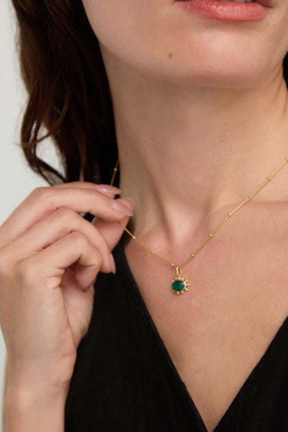 A woman wearing a black top gently holds the Gold Vermeil Green Onyx Necklace, featuring a faceted green onyx pendant, between her fingers.